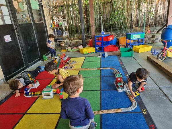 Preschoolers building a wooden train track on the classroom rug
