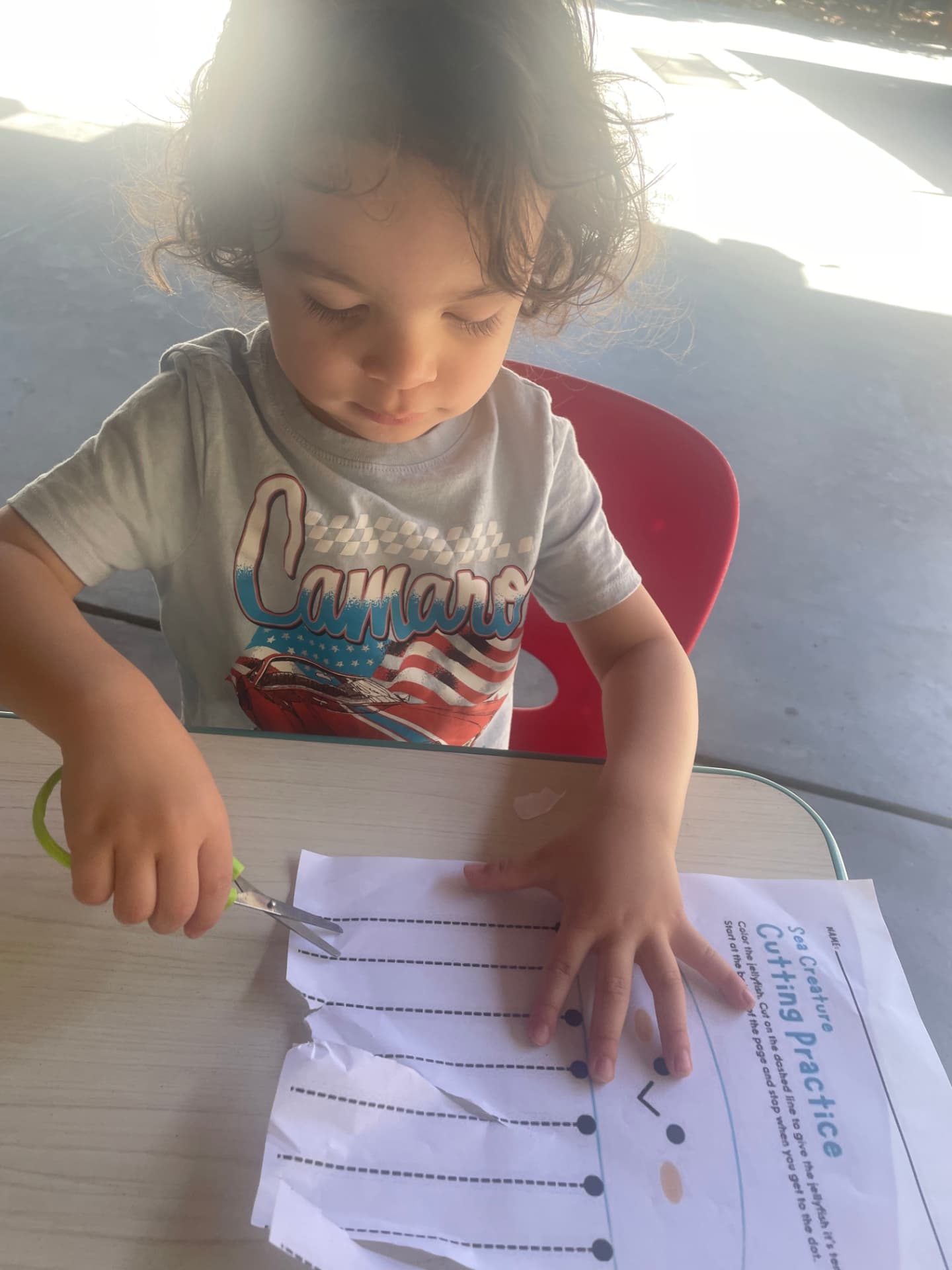 A preschooler practicing scissor skills on a cutting worksheet