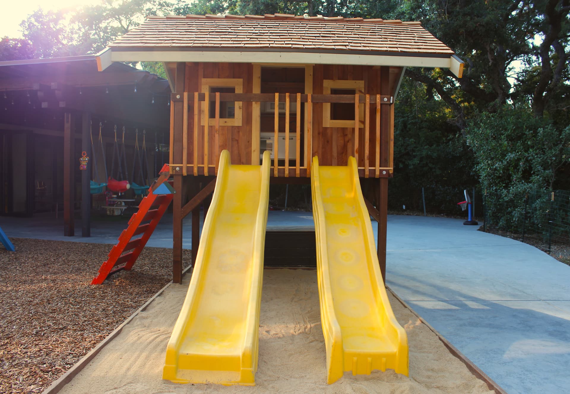 The wooden playhouse with two yellow slides over the sandbox