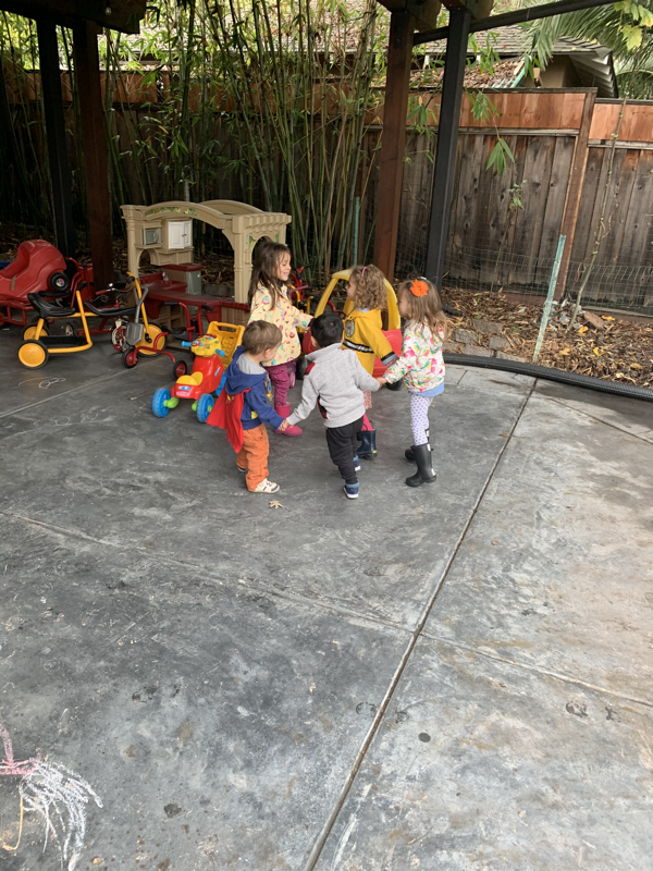 Children holding hands on the covered patio with riding toys