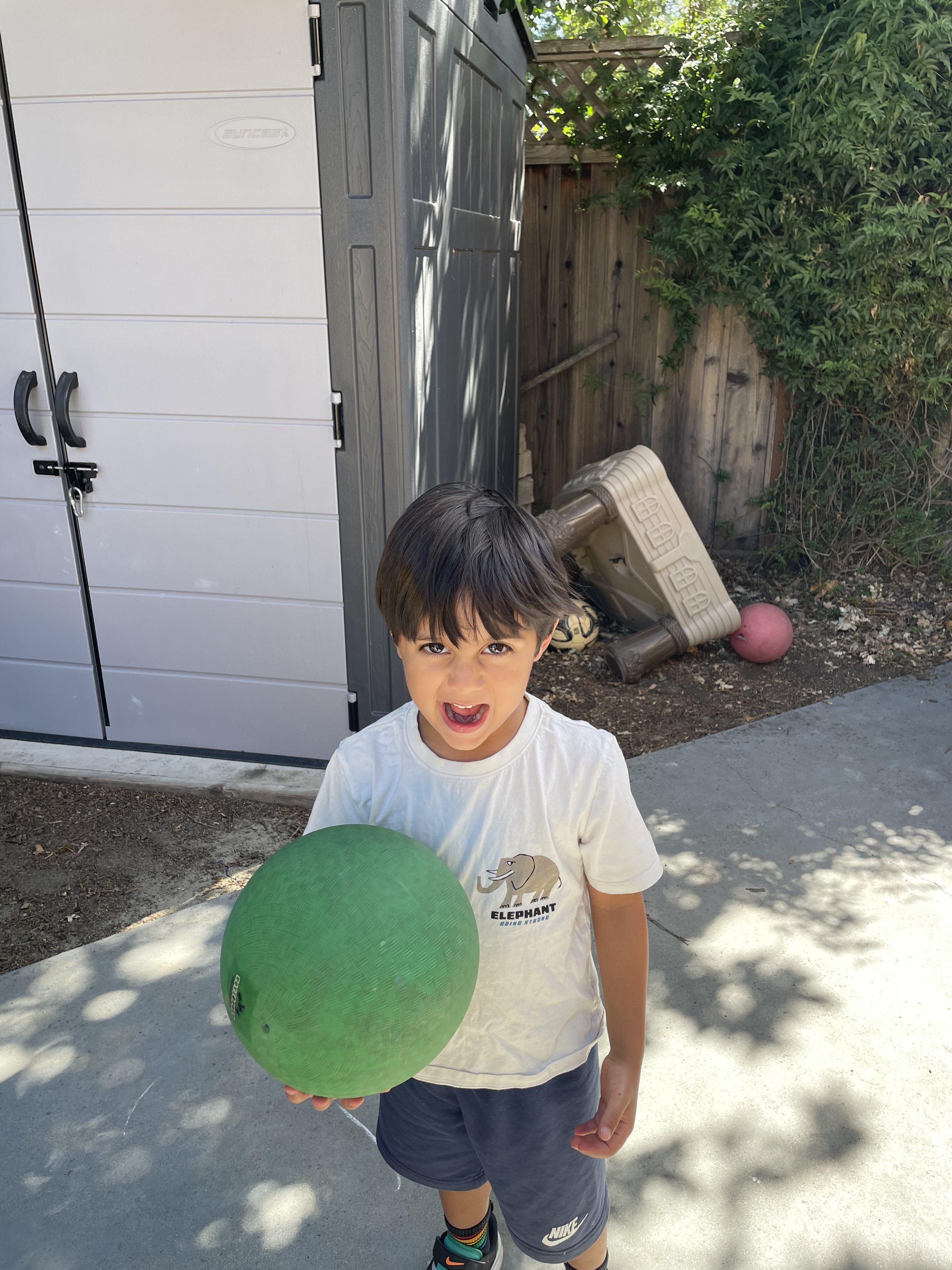 A preschooler playing with a green ball in the outdoor yard