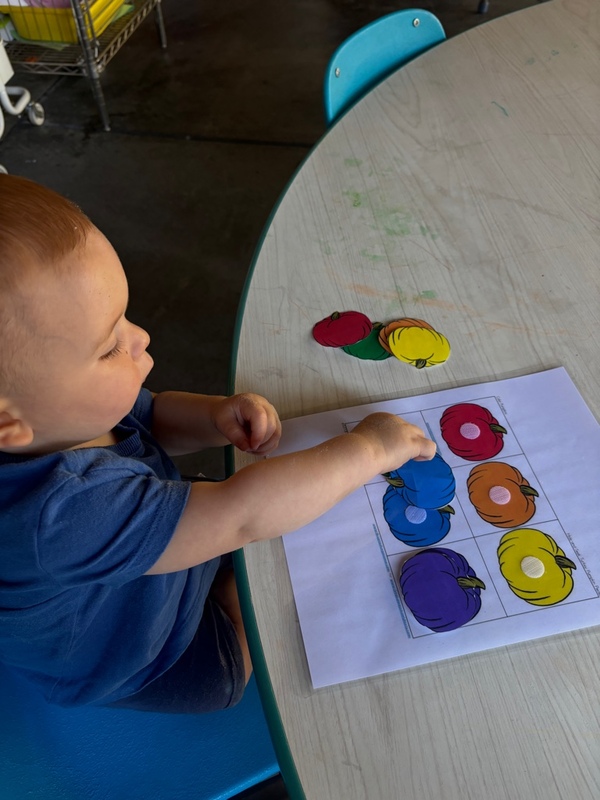 A toddler matching colorful pumpkins by color at the activity table