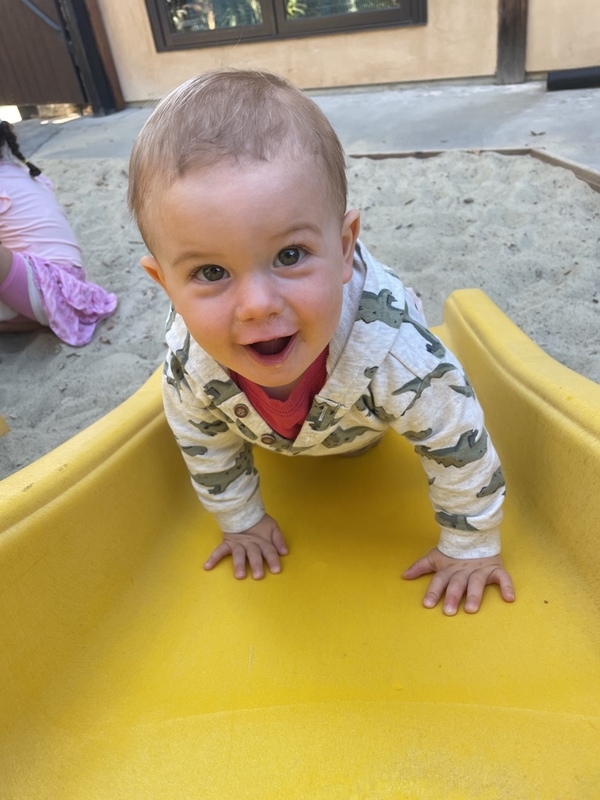 A toddler climbing the yellow slide in the sandbox play area