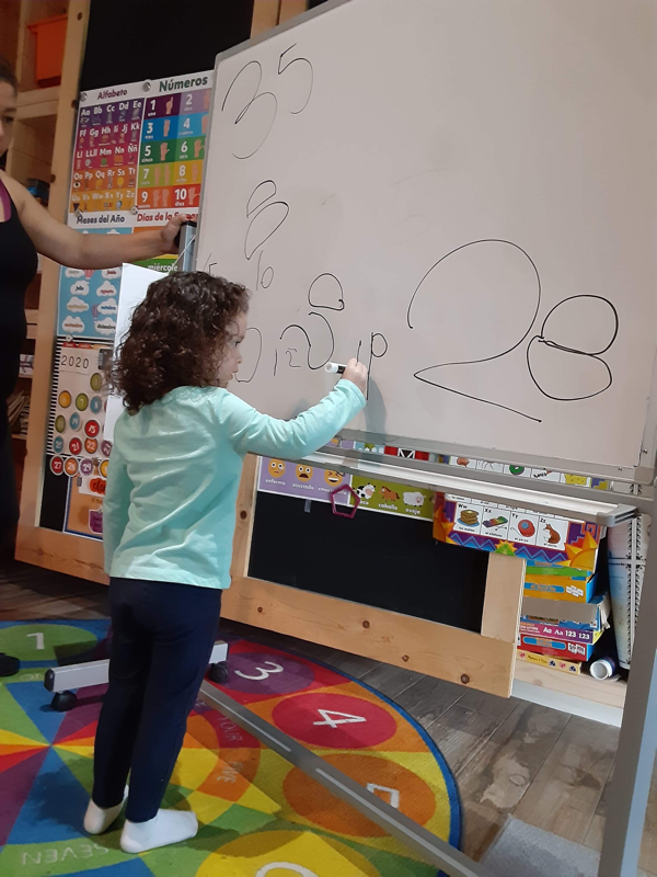 A preschooler practicing numbers on the whiteboard